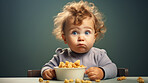 Toddler eating a bowl of cereal or snack. Messy funny boy eating and looking shocked