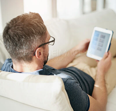 Buy stock photo Shot of a man using his tablet while relaxing on the sofa at home