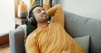 Music, headphones and asian man relax on a sofa with audio, streaming or track in his home. Earphones, radio and male with wellness app in a living room with podcast for resting, nap or day off peace