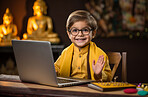 Portrait of buddhist boy sitting at table with laptop. Religion concept.