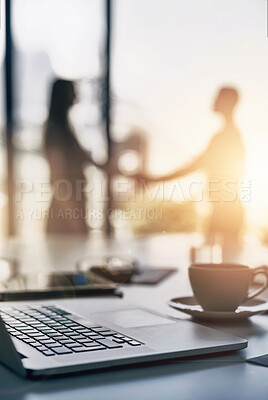 Buy stock photo Closeup shot of a laptop on a desk with businesspeople shaking hands in the background