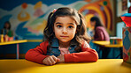 Portrait of a toddler girl sitting at a desk at kindergarten. Preschool and eduction