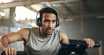 Asian man, headphones and cycling at gym on machine and listening to music in sports workout or exercise. Serious male person or athlete training on bicycle machine or equipment for healthy cardio