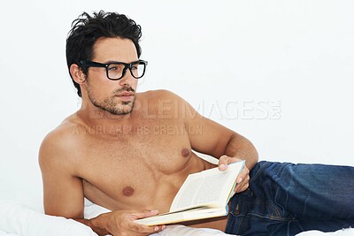 Buy stock photo Shot of a handsome young man lying on his bed reading a book