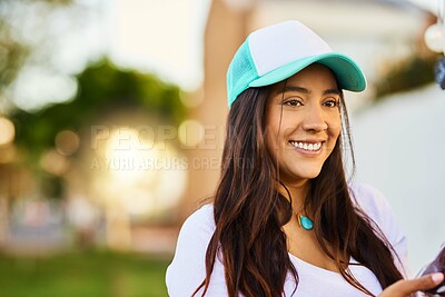 Buy stock photo Shot of a cheerful young woman wearing a hat while standing outside smiling