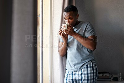 Buy stock photo Cropped shot of a handsome young man standing and looking contemplative in his bedroom while enjoying a cup of coffee