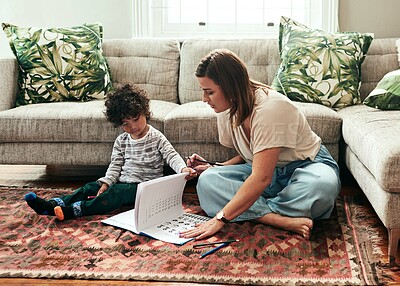 Buy stock photo Shot of a cheerful young woman and her son doing homework together while being seated on the floor in the living room