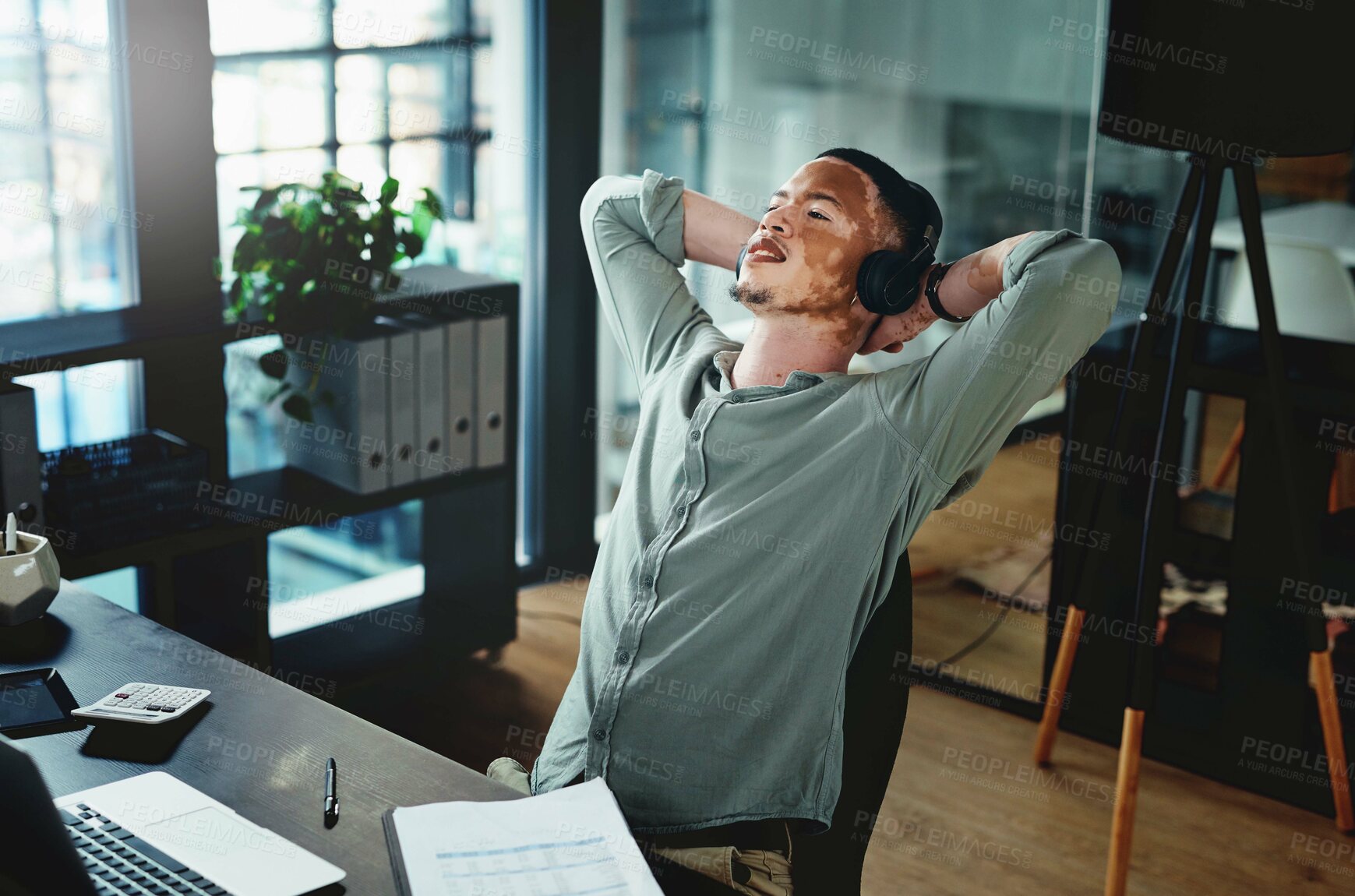 Buy stock photo Shot of a young businessman wearing headphones while taking a nap in an office