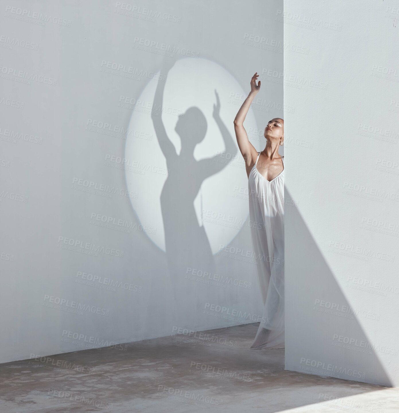 Buy stock photo Shot of an attractive young woman posing in a white dress against a spotlight