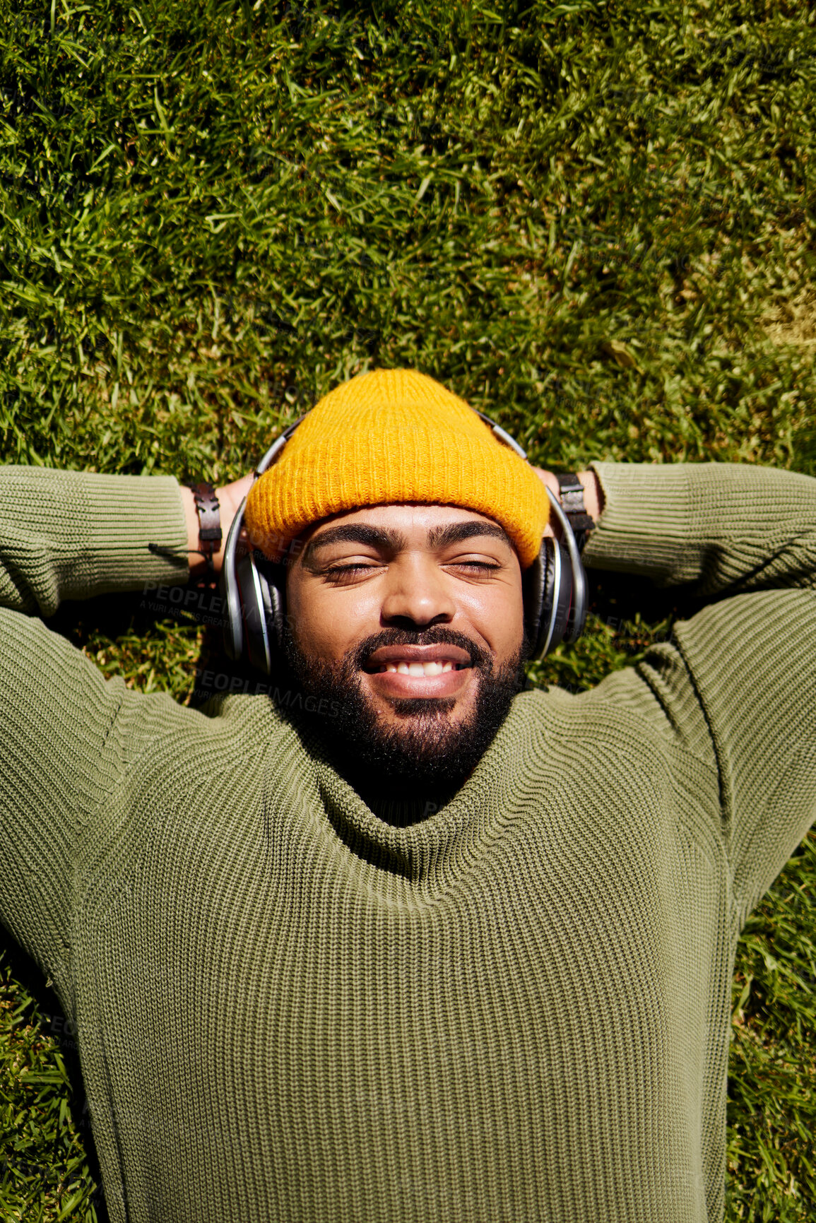 Buy stock photo Top view, headphones and man relax on grass outdoor, listening to music and audio online or hearing sound of podcast. Smile, streaming radio and person at park resting for peace, calm and freedom