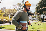 Man on campus, university books and headphones on morning commute for education with backpack. Learning, studying and college student in park with podcast, music or streaming online lecture on walk.