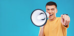 Megaphone, smile and portrait of man in studio pointing for announcement, speech or rally. Happy, protest and young person from Canada with bullhorn for loud communication isolated by blue background