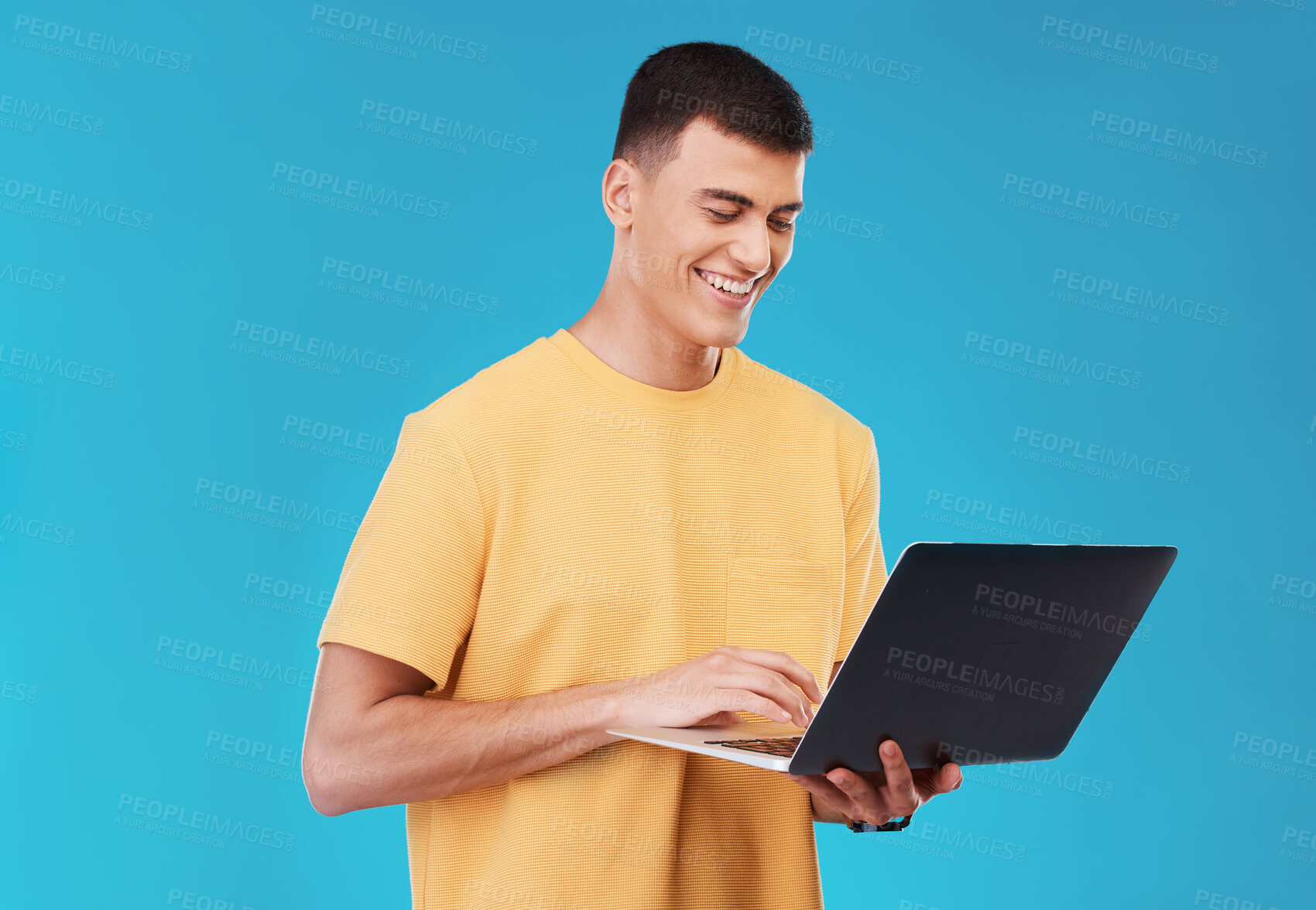 Buy stock photo Laptop, research and man student in a studio working on a university project on the internet. Smile, technology and young male person studying for college test or exam on computer by blue background.
