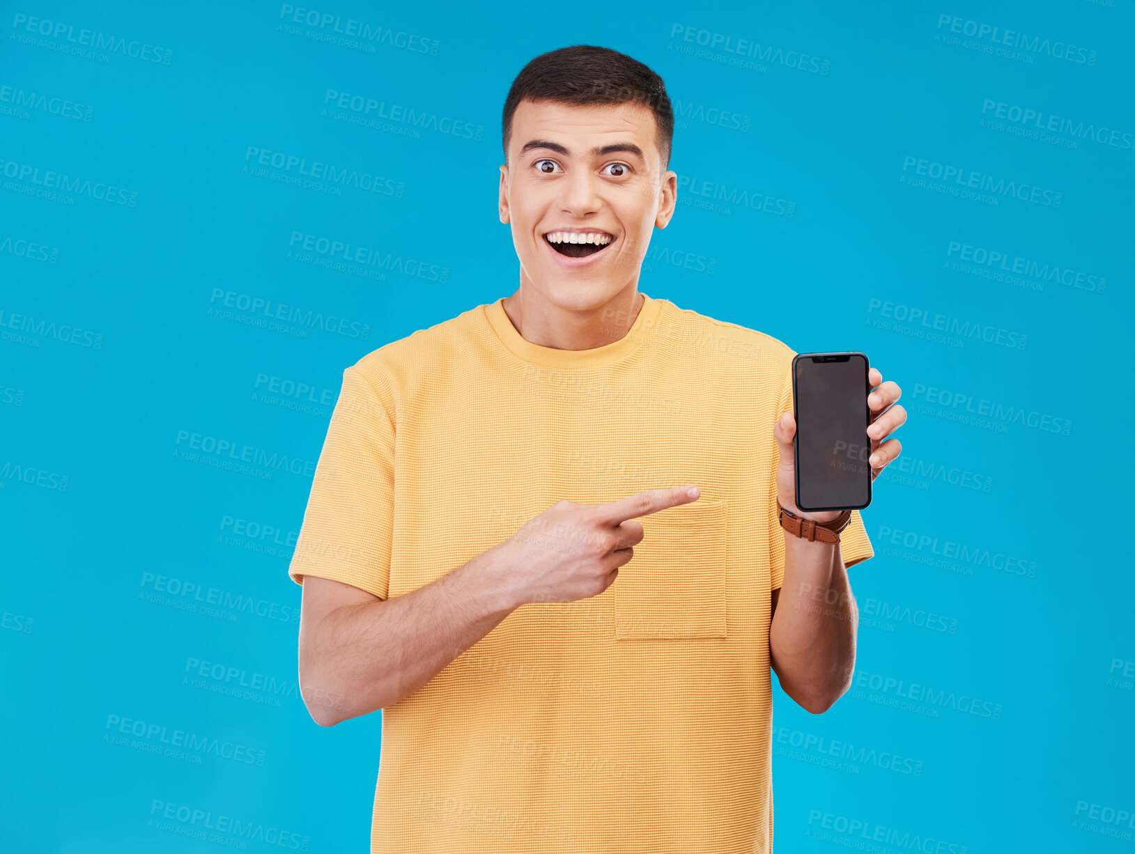 Buy stock photo Portrait, phone and pointing with an excited man on a blue background in studio for social media marketing. Contact, notification or alert with a happy young person showing a mobile screen or display