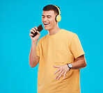 Phone, headphones and man singing in studio listening to music, radio or playlist for entertainment. Smile, technology and male person streaming song or album for karaoke isolated by blue background.