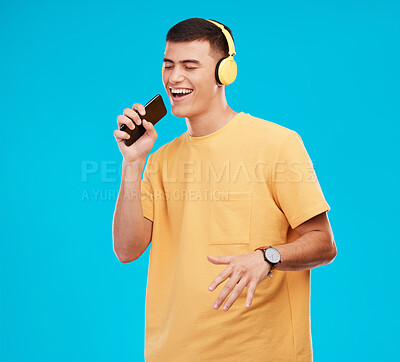 Buy stock photo Phone, headphones and man singing in studio listening to music, radio or playlist for entertainment. Smile, technology and male person streaming song or album for karaoke isolated by blue background.