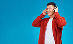 Man, smile and headphones for song on phone in studio by blue background. Asian person, listening and streaming the music, radio and audio or funny podcast on smartphone, technology and sound for joy