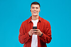 Man, earpods and smile with phone for communication in portrait, studio and happy by blue background. Asian male model, texting and chat on smartphone while streaming radio, song and audio or podcast