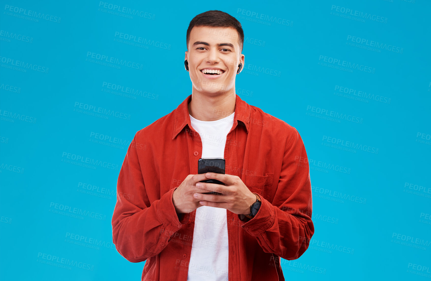 Buy stock photo Man, earphones and smile with phone for communication in portrait, studio and happy by blue background. Asian male model, text and chat on smartphone while streaming music, song and audio or podcast