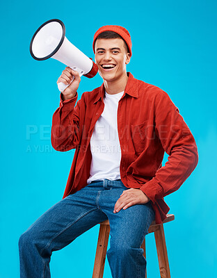Buy stock photo Portrait, megaphone and young man in a studio for an announcement or speech for a rally. Happy, smile and male activist on stool with bullhorn for loud communication isolated by blue background.