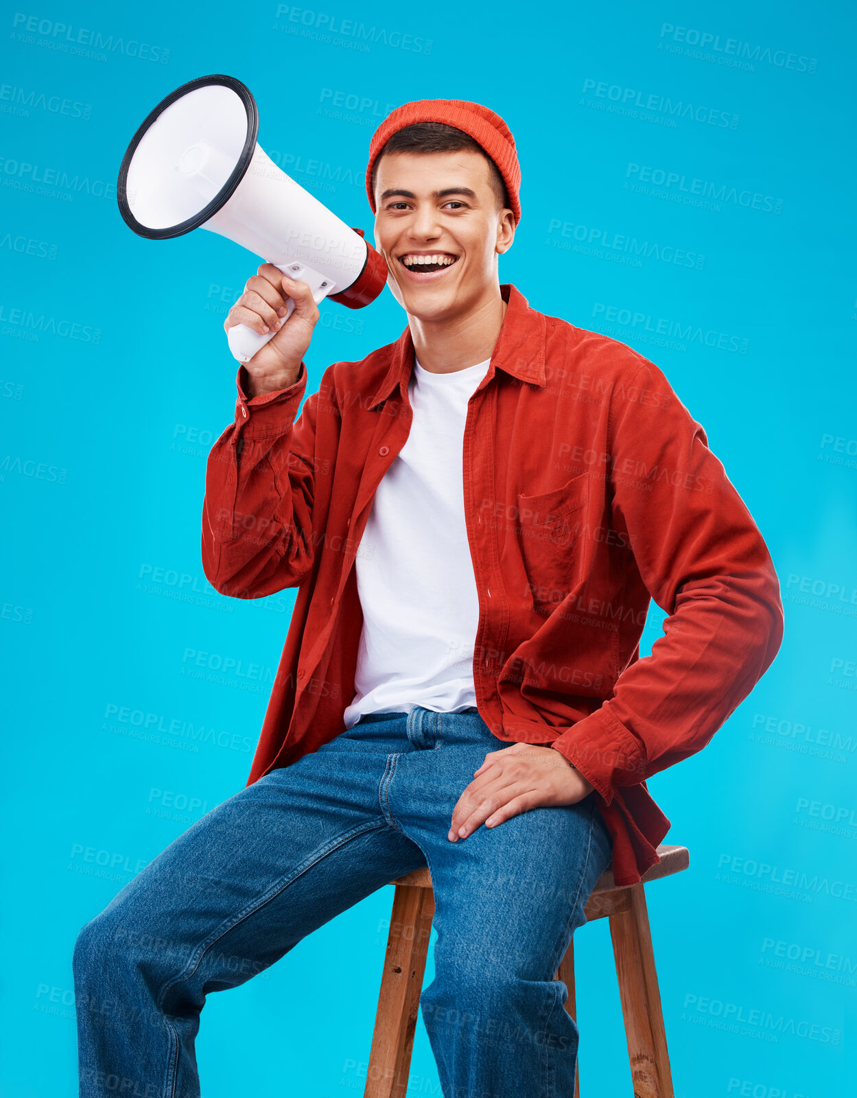 Buy stock photo Portrait, megaphone and young man in a studio for an announcement or speech for a rally. Happy, smile and male activist on stool with bullhorn for loud communication isolated by blue background.