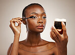 Black woman, mascara with brush and mirror for beauty, makeup and shine isolated on brown background. Eyelash extension, wand and skin glow with cosmetology, transformation and wellness in studio