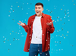 Portrait, confetti and man with celebration, achievement and excited on a blue background. Person, guy and model with sparkle, success and happiness with surprise, wow and omg with victory or winning