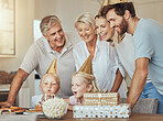 Parents, grandparents and children at birthday with cake in celebration with sweets, love and gift in home. Happiness, men and women together at table at kids party in house with girl blowing candles