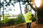 Senior man, running and listening to music on road in nature, countryside or forest with water bottle in exercise. Fitness, training and workout or speed run in woods for cardio, health and wellness