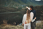 Couple, relax and pointing to mountain for hiking, camping or nature for outdoor scenery together. Rear view of man and woman hug enjoying holiday vacation,  travel trip or trekking adventure outside