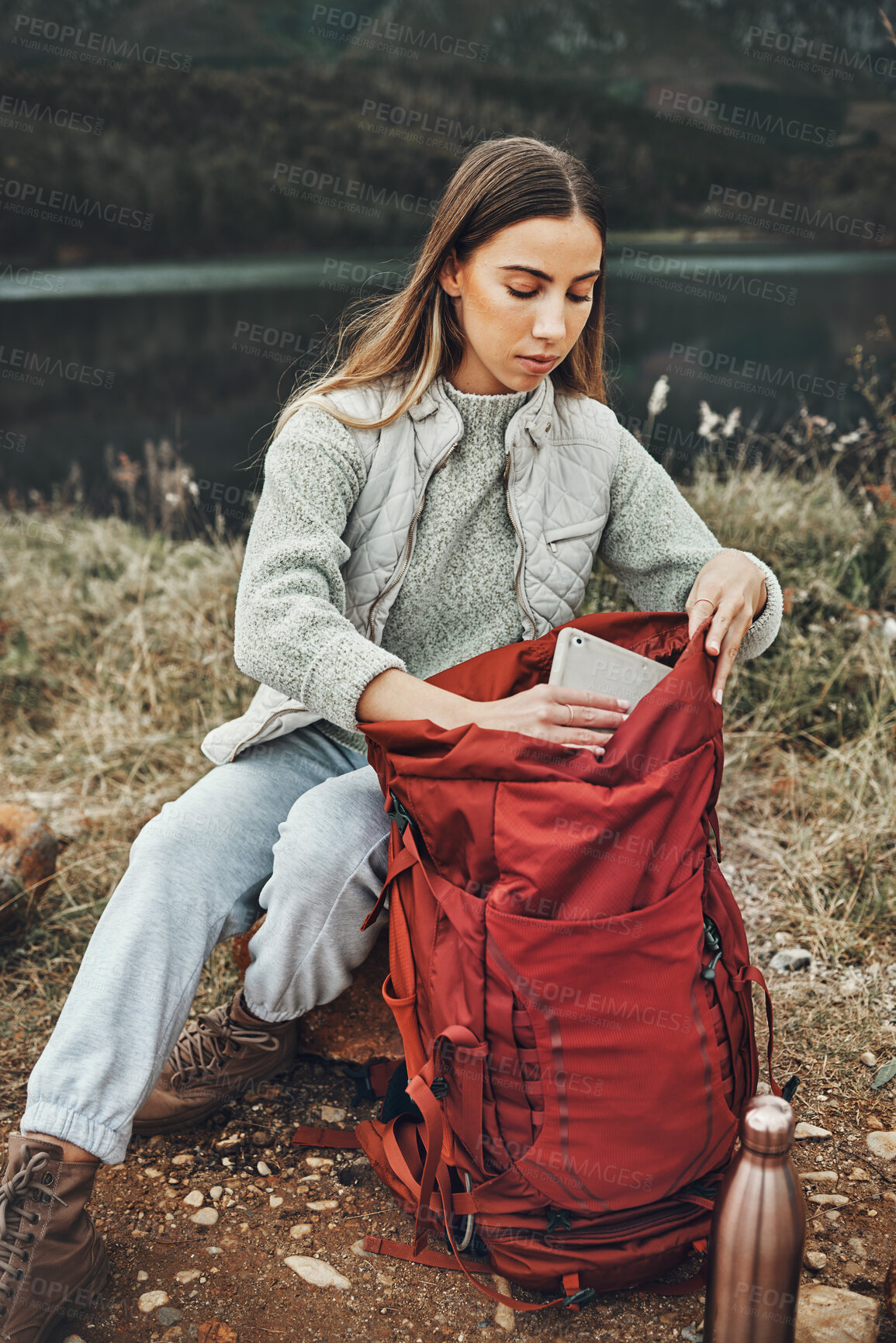 Buy stock photo Woman, hiking and packing backpack in nature with tablet, check and thinking by lake, mountain or outdoor. Girl, luggage and trekking with bad, technology and ideas on adventure in countryside