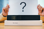 Books, stack and closeup on desk for faith, Abrahamic religion and question mark on poster for study in home. Person, holy spirit and education for choice with Jesus, Moses and worship God with sign