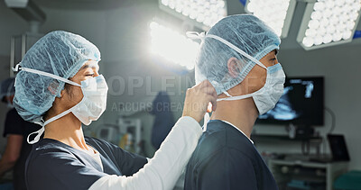 Surgery, hospital and doctors tie mask in operating room for medical service, preparation and operation. Healthcare team, safety scrubs and people with uniform for emergency, procedure and protection