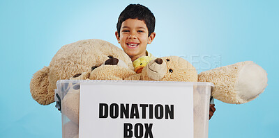 Boy in studio with toys, donation in box and smile for children, social charity and hope in kindness. Care, donate and happy kindergarten child with teddy bear package at kids ngo on blue background.