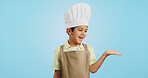 Child, happy face and chef hand to show promotion, advertising or deal in studio. Dress up, profession and young boy happy from future career of cooking and open palm for sale with blue background