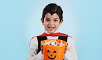 Halloween, basket and portrait of child with sweets or candy isolated in a studio blue background and happy. Holiday, laughing and kid in vampire costume for celebration in fantasy festival of horror