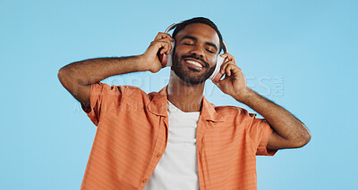 Black man, headphones and dancing to music with happiness and energy in studio on blue background. Techno, rave and fun with audio streaming, dancer is excited with smile and wireless technology