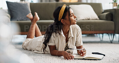 Thinking, writing in book and woman on floor in living room at home for creative idea, problem solving or planning vision. Serious, inspiration and Indian person with journal for notes, list or study