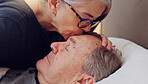 Senior woman kissing her husband on forehead with love, care and marriage in bed at home. Sick, recovery and elderly couple in retirement with illness in bedroom of hospice, nursing center or house.