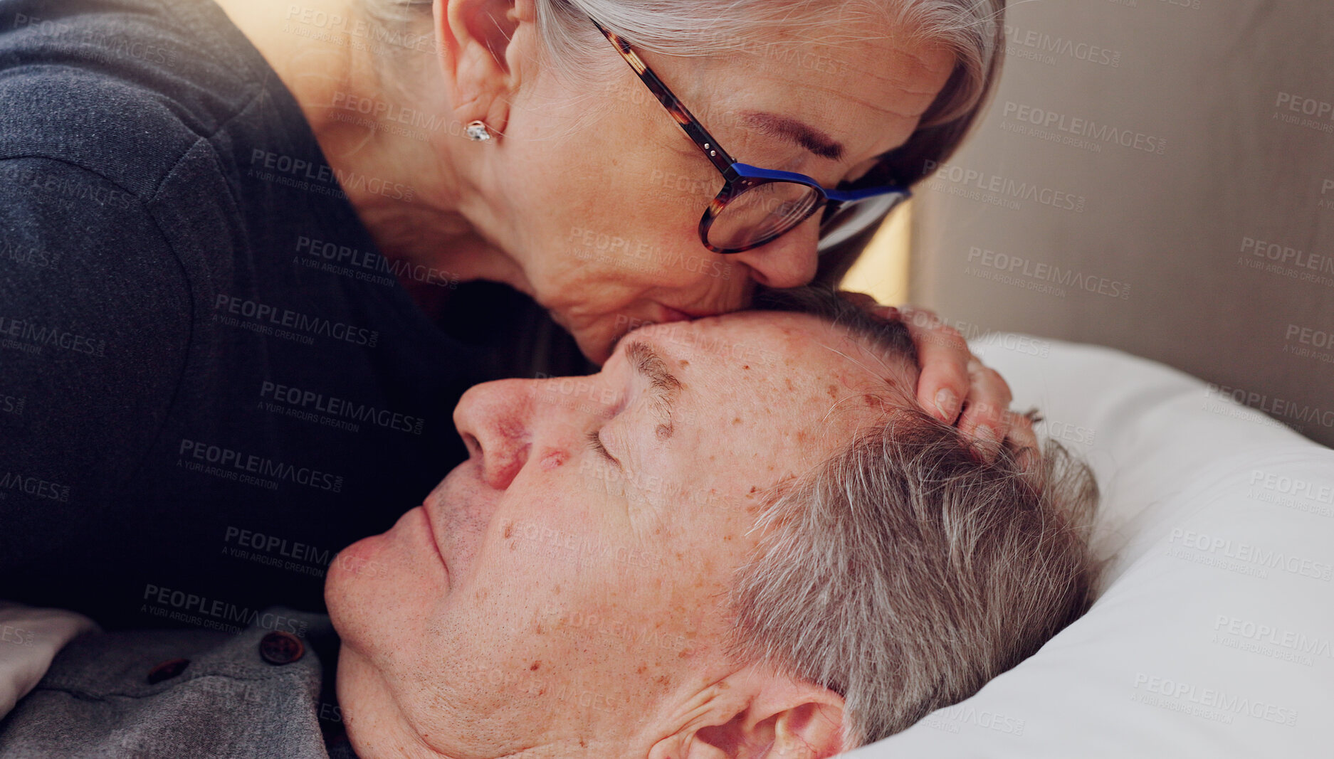Buy stock photo Senior woman kissing her husband on forehead with love, care and marriage in bed at home. Sick, recovery and elderly couple in retirement with illness in bedroom of hospice, nursing center or house.