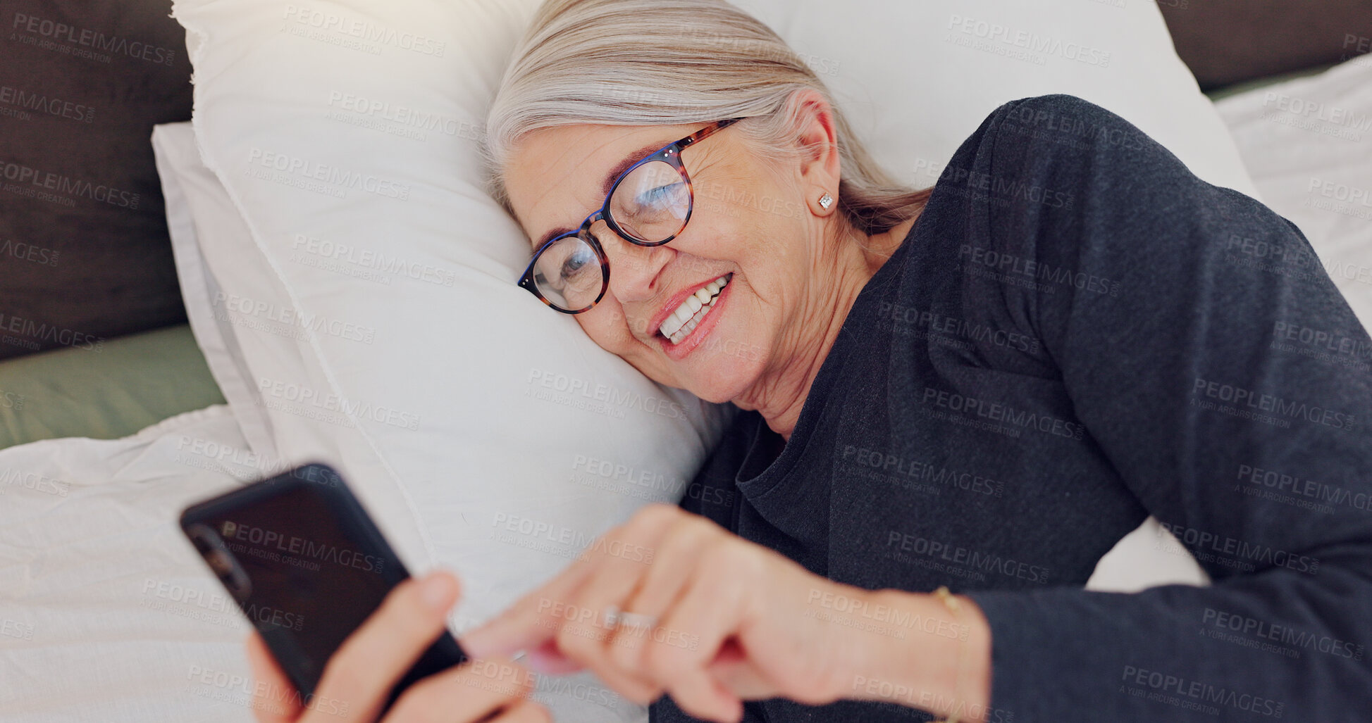 Buy stock photo Happy, senior woman and reading with phone in bed or streaming funny, comedy or meme on social media. Elderly person, smile or relax with cellphone at night in bedroom with communication or chat