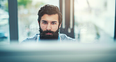 Buy stock photo Shot of a young businessman using a computer at his desk in a modern office
