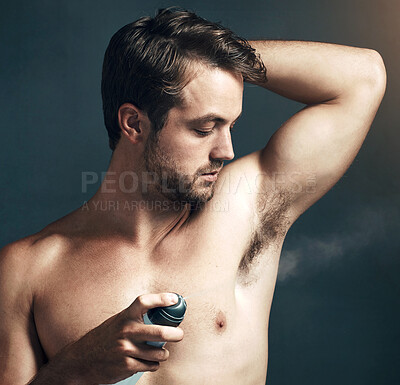 Buy stock photo Cropped shot of a handsome young man spraying deodorant on his armpit