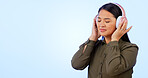 Woman, headphones and listening to music or podcast, audio and song in studio by blue background. Asian female model, hearing and streaming radio, sound and playlist for peace, chilling and mockup
