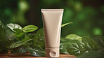 Beige blank tube container on a green leafy backdrop. For organic or eco friendly product