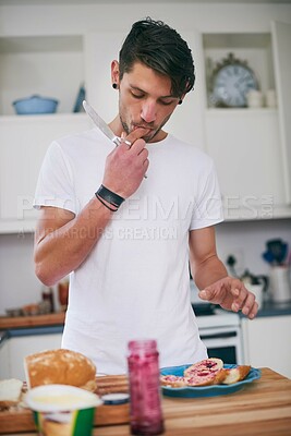 Buy stock photo Shot of a handsome young man standing in his kitchen making a sandwich
