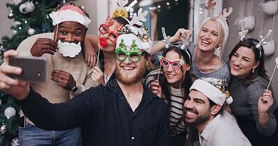 Buy stock photo Shot of a group of young friends wearing funny hats and taking selfies at a Christmas party