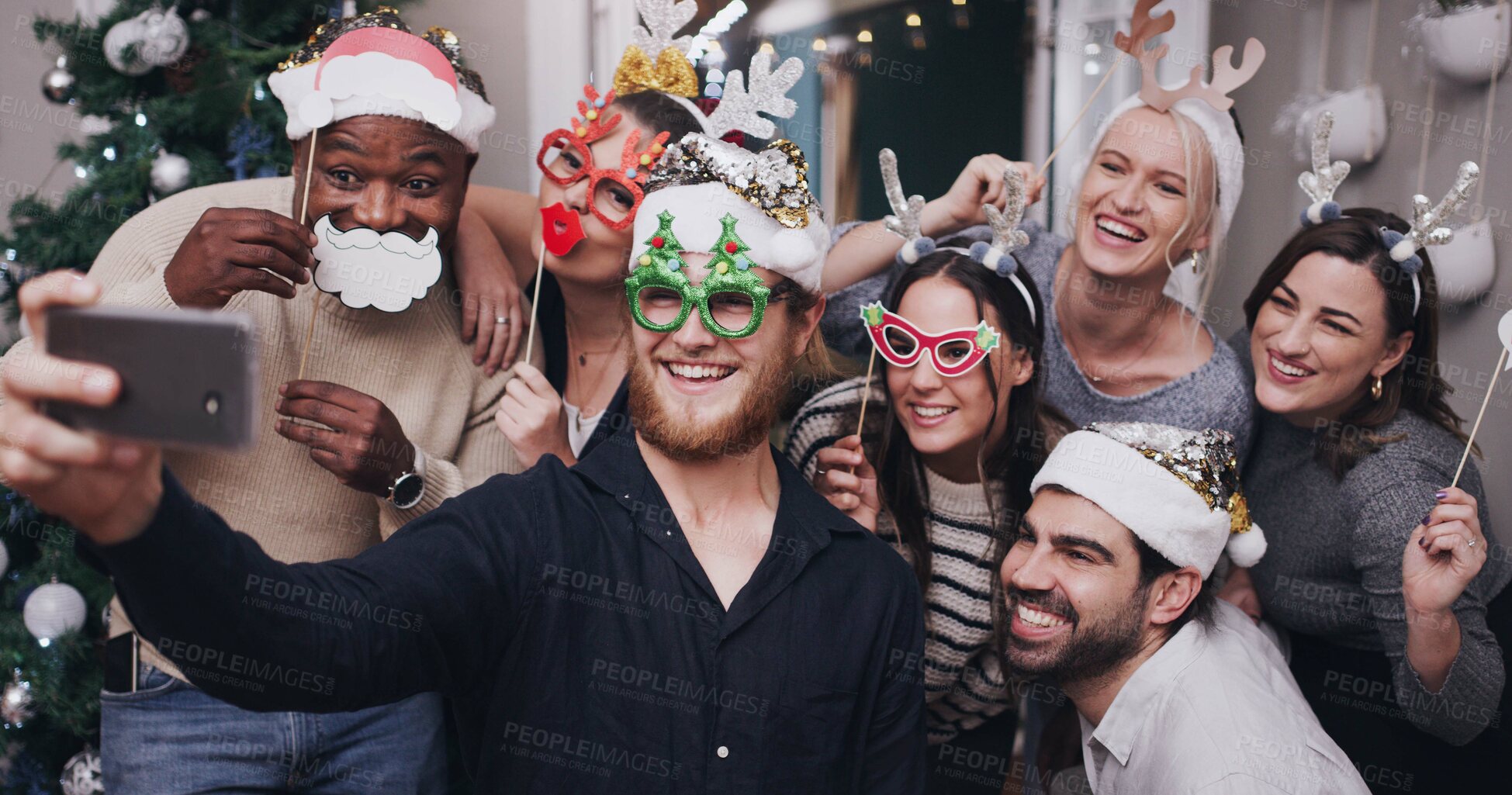 Buy stock photo Shot of a group of young friends wearing funny hats and taking selfies at a Christmas party