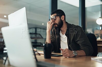 Buy stock photo Shot of a young businessman feeling stressed while working late at night in a modern office