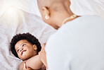 Love, bonding and mother playing with baby on bed relaxing and playful together in nursery at home. Happy, maternal and young African mom with little newborn, child or kid in bedroom at modern house.